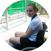 Photo of a young girl using a wheelchair outside, looking towards the camera