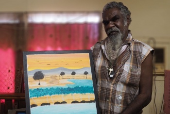 An Aboriginal man is holding a painting of the Australian landscape.