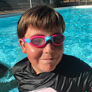 NDIS participant, Christopher, in a pool, wearing pink goggles. Christopher is smiling at the camera.