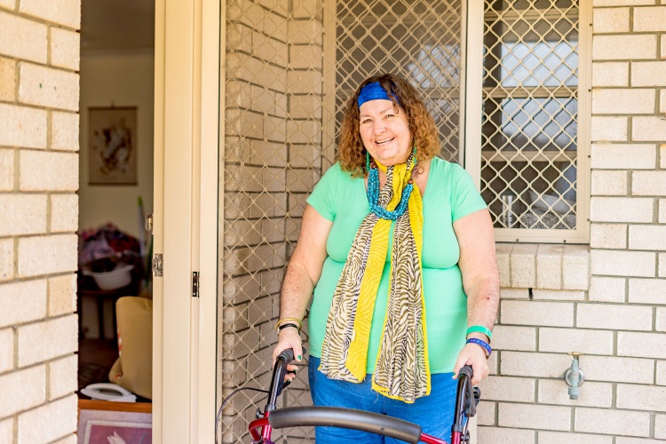 Michelle stands smiling in the doorway of her house with her walker