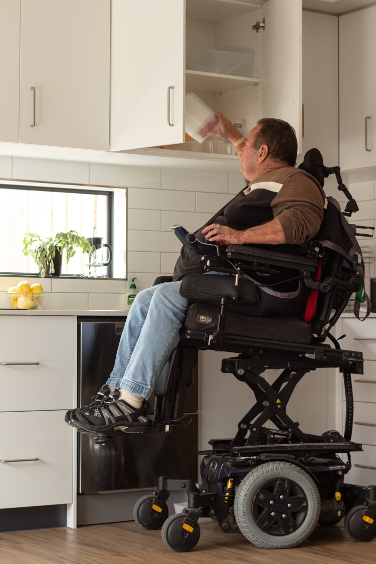 Brenton Bell using his wheelchair to reach high cupboards
