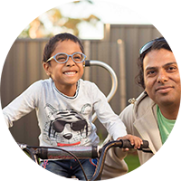 Photo of a young boy on his bike smiling at the camera with his father by his side