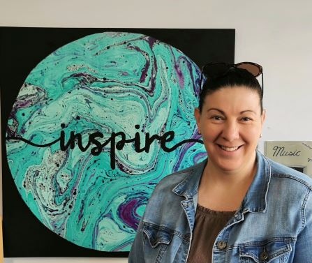 Melissa Sutczak standing in front of a beautiful piece of art that says 'Inspire'.