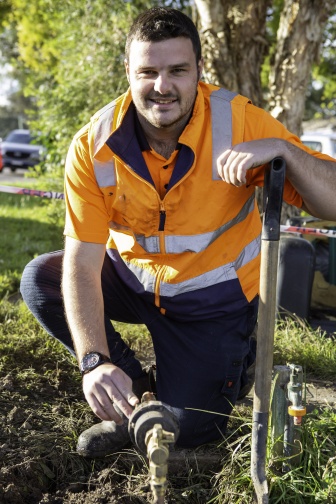 NDIS participant Sam at work plumbing a water connection looking at the camera