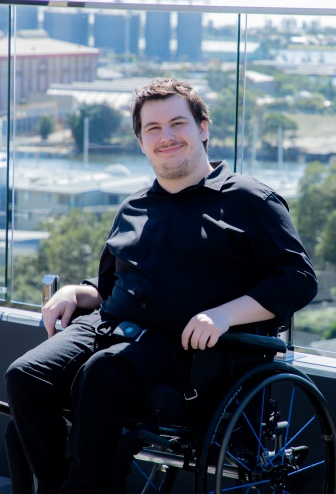 A young man in a wheelchair is on a rooftop courtyard smiling.