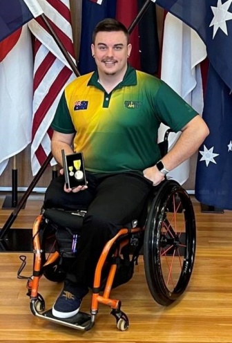 Braedon in his wheelchair wearing an Australian rugby top in front of the American flag.