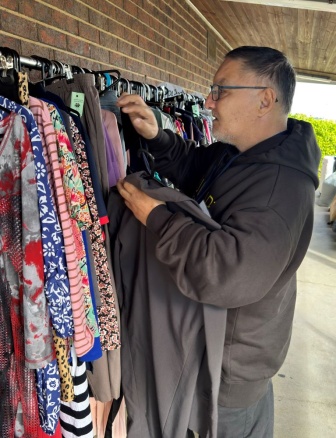 Man in black hoodie hangs clothes on rack at op shop.