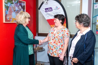 Elise is standing and shaking hands with her local area coordinator. Next to Elise, her mother stands looking proud.