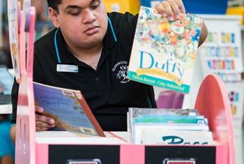21-year-old male NDIS participant and School Leaver Employment Supports recipient, happily sorting classroom readers at a child's desk, one of the many tasks he is employed to do.