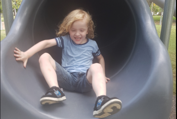 Young male NDIS participant coming down an enclosed slide smiling.