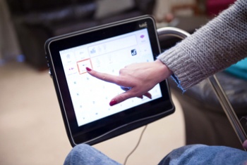 NDIS participant touches an icon on her screen to communicate.