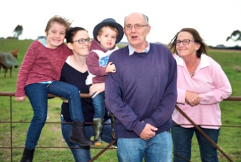 Four-year-old male NDIS participant, his mum, sister, nan and pop all sit and lean on a farm fence with horses in the background.