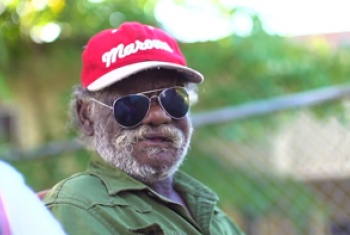 Older Indigenous NDIS participant with a red and white hat and sunglasses enjoying the outdoors.