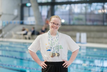 Lily stands in front of the pool with her swimming medals