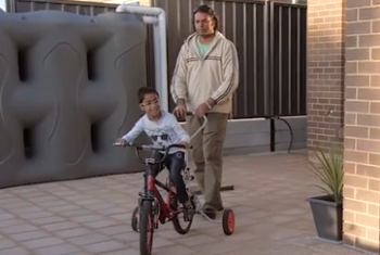 Ram enjoys riding his bike in his yard at home with his dad's help