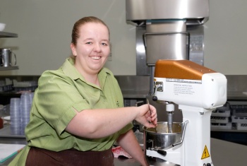 Martika smiling wears a green button shirt manning a mixer at her job