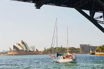A yacht sails under the Sydney Harbour Bridge, the Sydney Opera House is in the distance