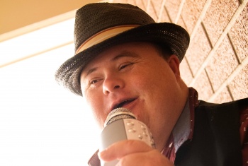 Stanley singing into a hand-held microphone wearing a smart, black hat.