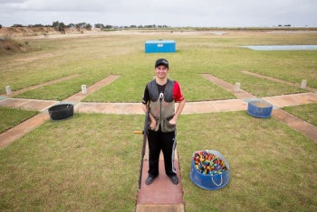 A man is standing on an outdoor clay shooting range holding a rifle.