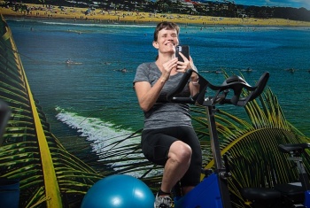 Chrystal on a gym exercise bike and holding a mobile phone