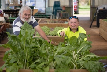 Jon Moore and Joel Bradley stand behind a raised garden bed of green vegetables