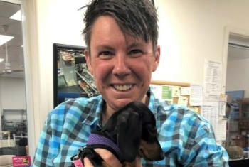 Smiling women in checked blue shirt holding small black dog against her