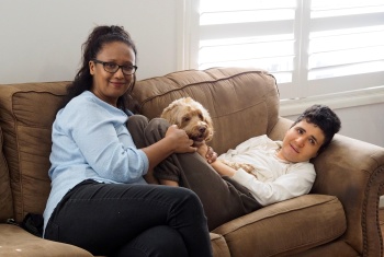 Jaden lying on a couch with his pet dog, Tanya is sitting beside Jaden, her arm over the dog and the other over Jaden.