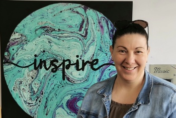 Melissa Sutczak standing in front of a beautiful piece of art that says 'inspire'.